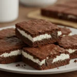 Close-up of fudgy, moist cottage cheese brownies on a plate, showcasing rich chocolate texture, glossy sheen, and visible dark chocolate chunks, with crumbs scattered around.